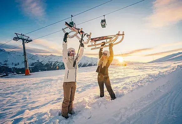 Two friends carrying their sledges overhead at the top of the Wildkogel gondola